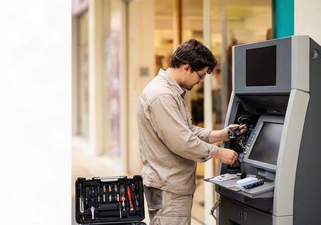 Singapore ATM technician checking a cash machine beside a retail entrance with service tools ready